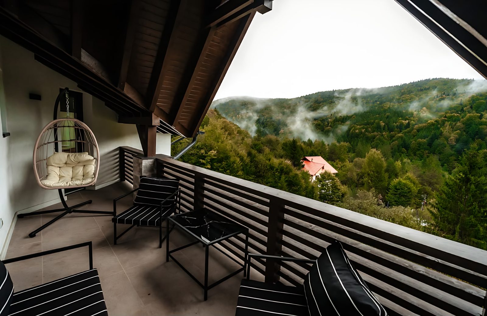 Balcon cu scaun suspendat și vedere spre pădure